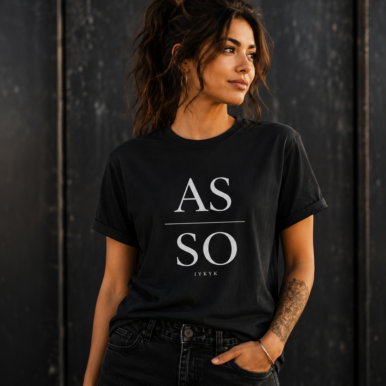 Woman wearing black As Above So Below IYKYK t-shirt against a dark textured background.